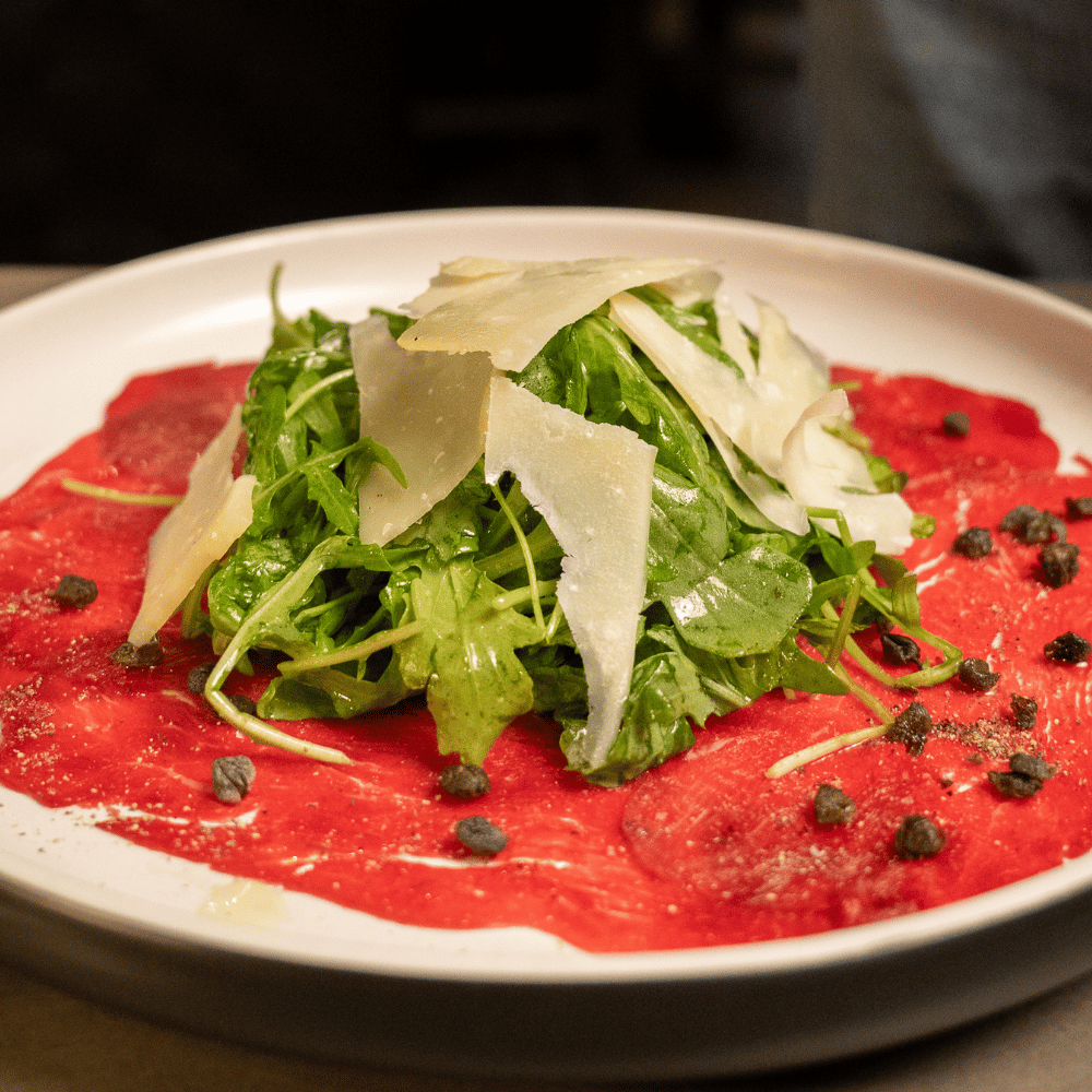 Plated dish with red sauce, arugula, and parmesan on a white plate.